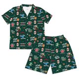 A matching two-piece sleepwear set consisting of a short-sleeve collared shirt and shorts, both in dark green with an all-over Christmas-themed print featuring Santa Claus, reindeer, gift boxes, trees, and text including 'A Griswold Christmas' and 'DAD, THE GIFT, AND CHRISTMAS'.