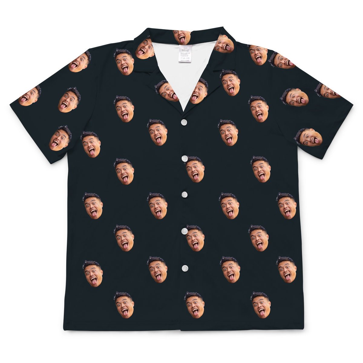 A short-sleeved, button-up pajama or casual shirt in a solid black or dark navy blue fabric. Repeated headshots of a person's highly expressive face, with their mouth wide open and tongue sticking out, are evenly spaced and superimposed across the fabric.