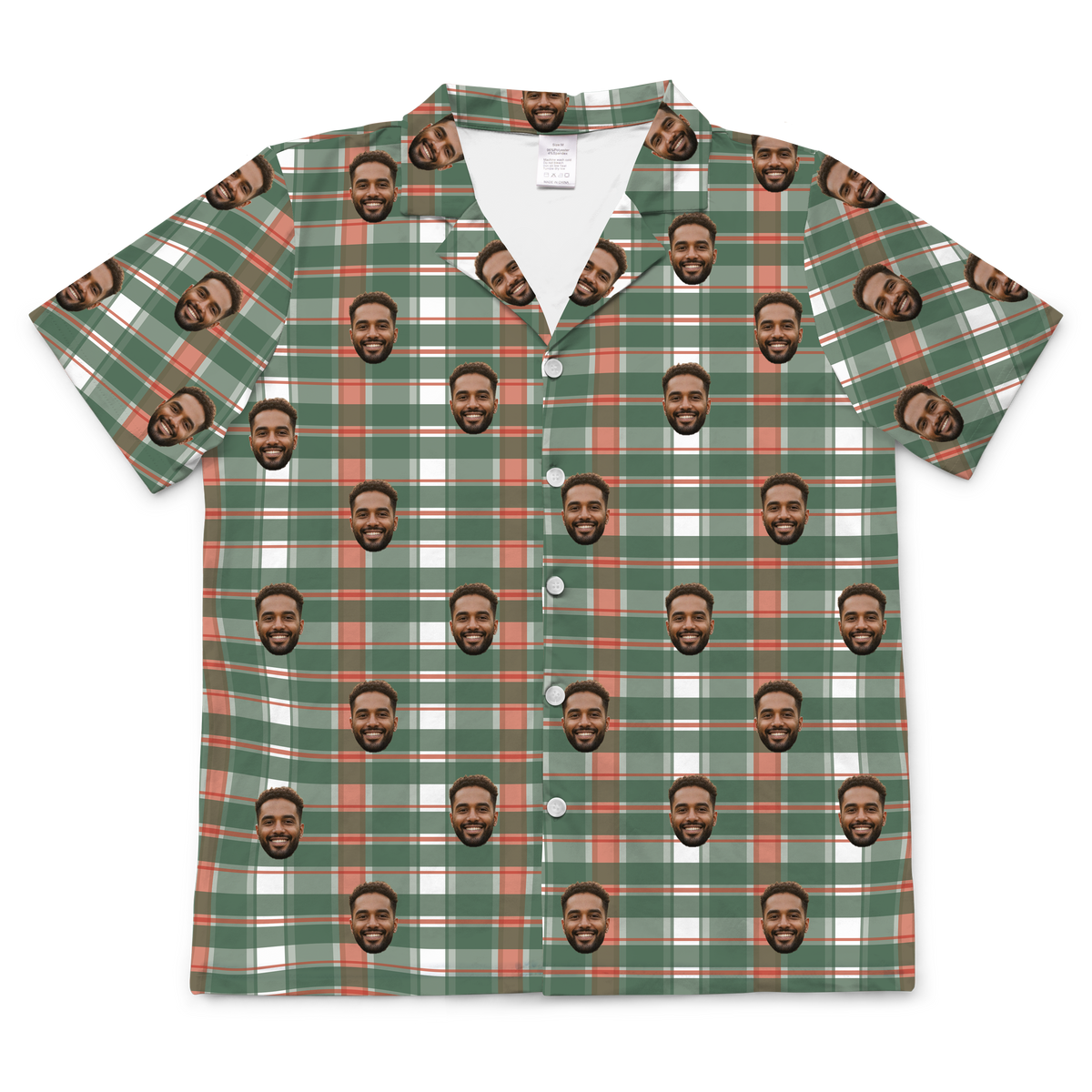 A short-sleeved, button-up pajama or casual shirt featuring a plaid or flannel-style pattern in green, white, and red/rust colors. Repeated headshots of a smiling, bearded man's face are superimposed onto the plaid fabric.