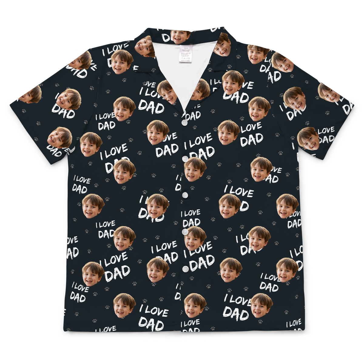 A short-sleeved, button-up pajama or casual shirt featuring a navy blue or dark gray background. The fabric is patterned with the repeating white text "I LOVE DAD" and small light gray paw prints. Repeated headshots of a young boy's smiling face are superimposed onto the pattern.