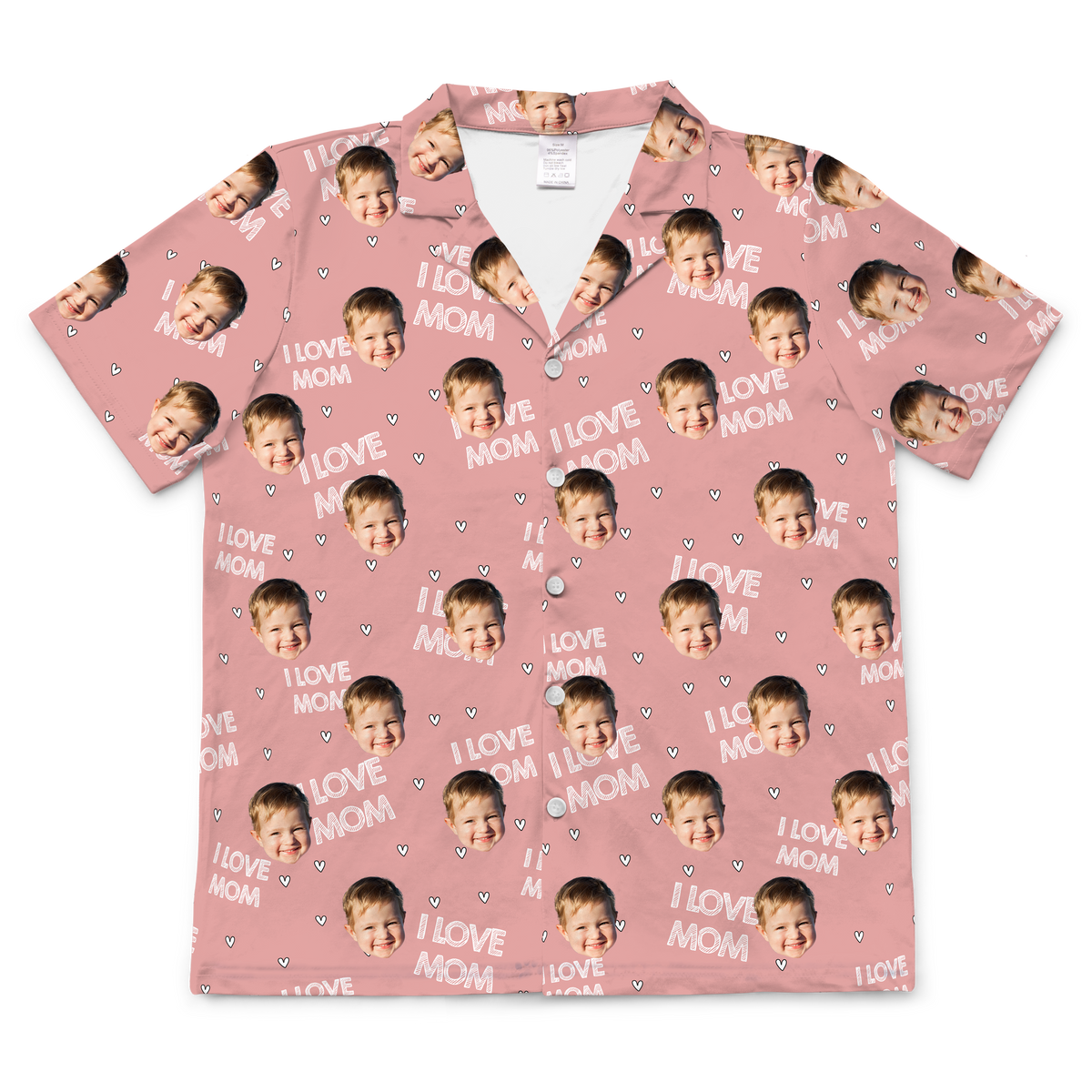 A short-sleeved, button-up pajama featuring a light pink or blush-colored background. The fabric is patterned with the repeating white text "I LOVE MOM" and small white heart outlines. Repeated headshots of a young boy's smiling face are superimposed onto the pattern.