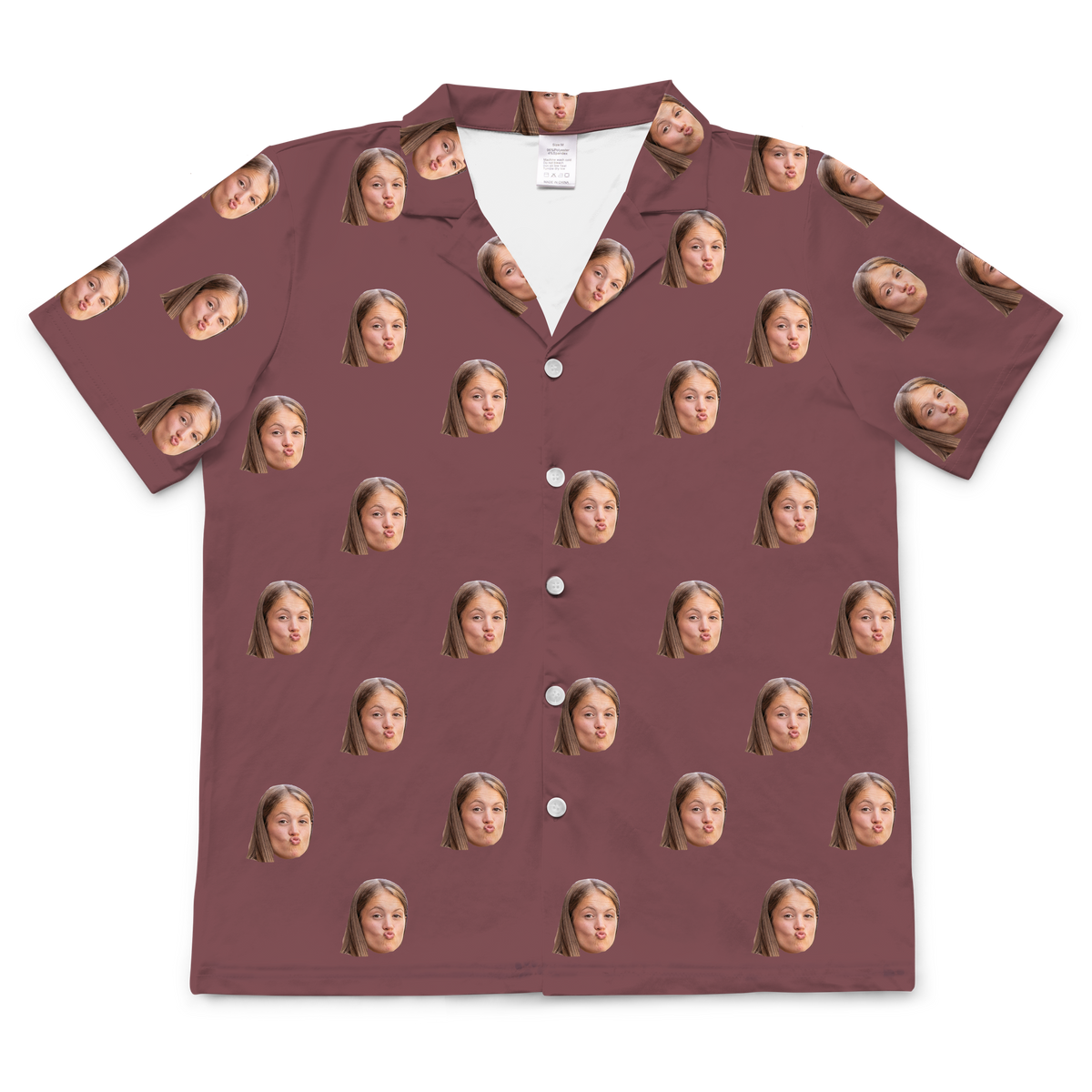 A short-sleeved, button-up pajama in a solid maroon or dusty rose-colored fabric. Repeated headshots of a young girl's face, making a playful 'fish face' or blowing a kiss, are evenly spaced and superimposed across the fabric.