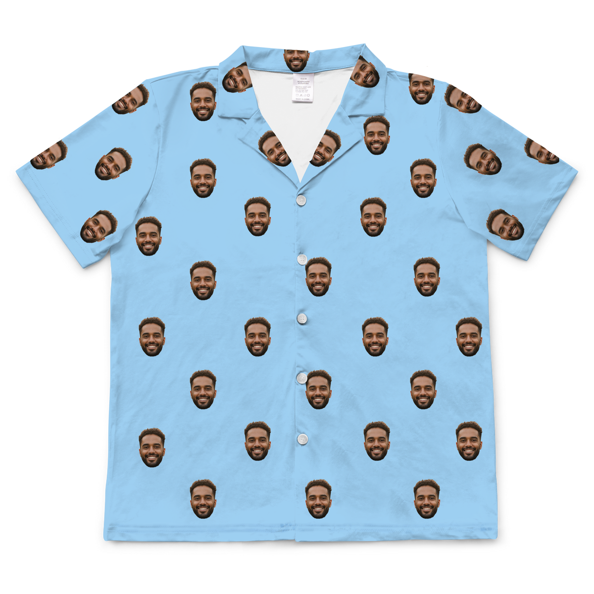 A short-sleeved, button-up pajama in a solid sky blue fabric. Repeated headshots of a smiling, bearded man's face are evenly spaced and superimposed across the fabric. 