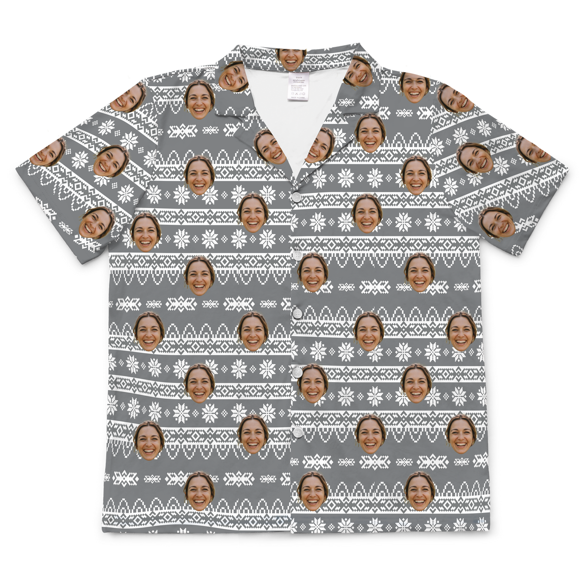 A short-sleeved, button-up pajama or casual shirt featuring a gray background patterned with a white, Nordic-style fair isle design, including stripes, crosses, and snowflakes, resembling a holiday sweater pattern. 