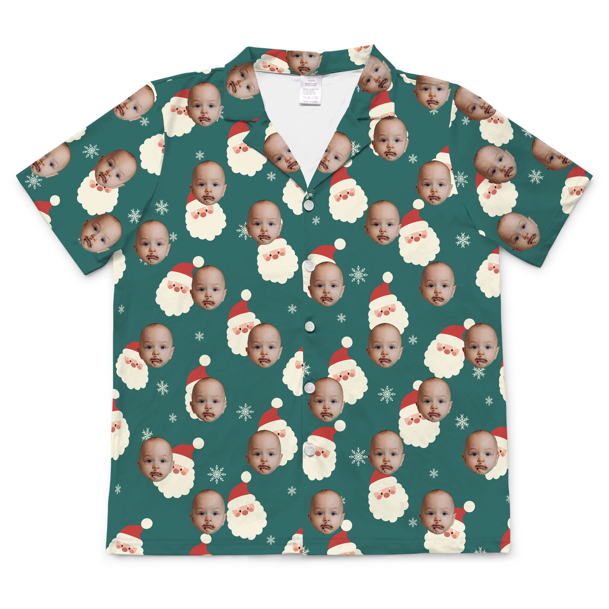 A short-sleeved, button-up pajama or casual shirt featuring a dark teal or evergreen background. The fabric is patterned with repeating graphics of Santa's face with a red hat and white beard, interspersed with white snowflakes.