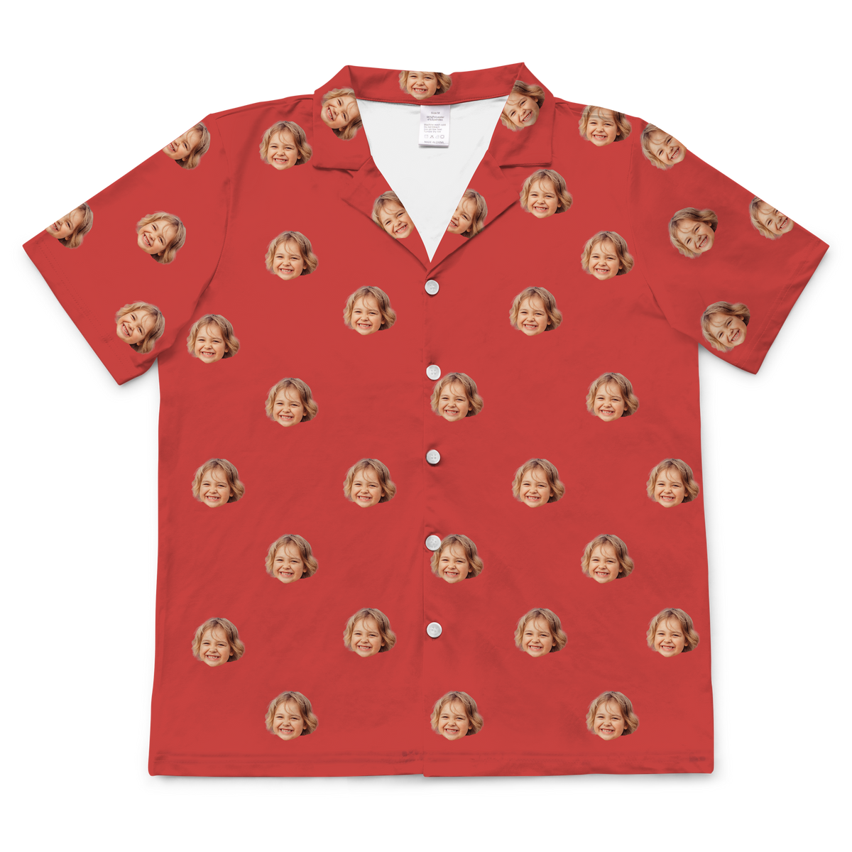 A short-sleeved, button-up pajama or casual shirt in a solid bright red fabric. Repeated headshots of a young blonde girl's smiling face are evenly spaced and superimposed across the fabric. 