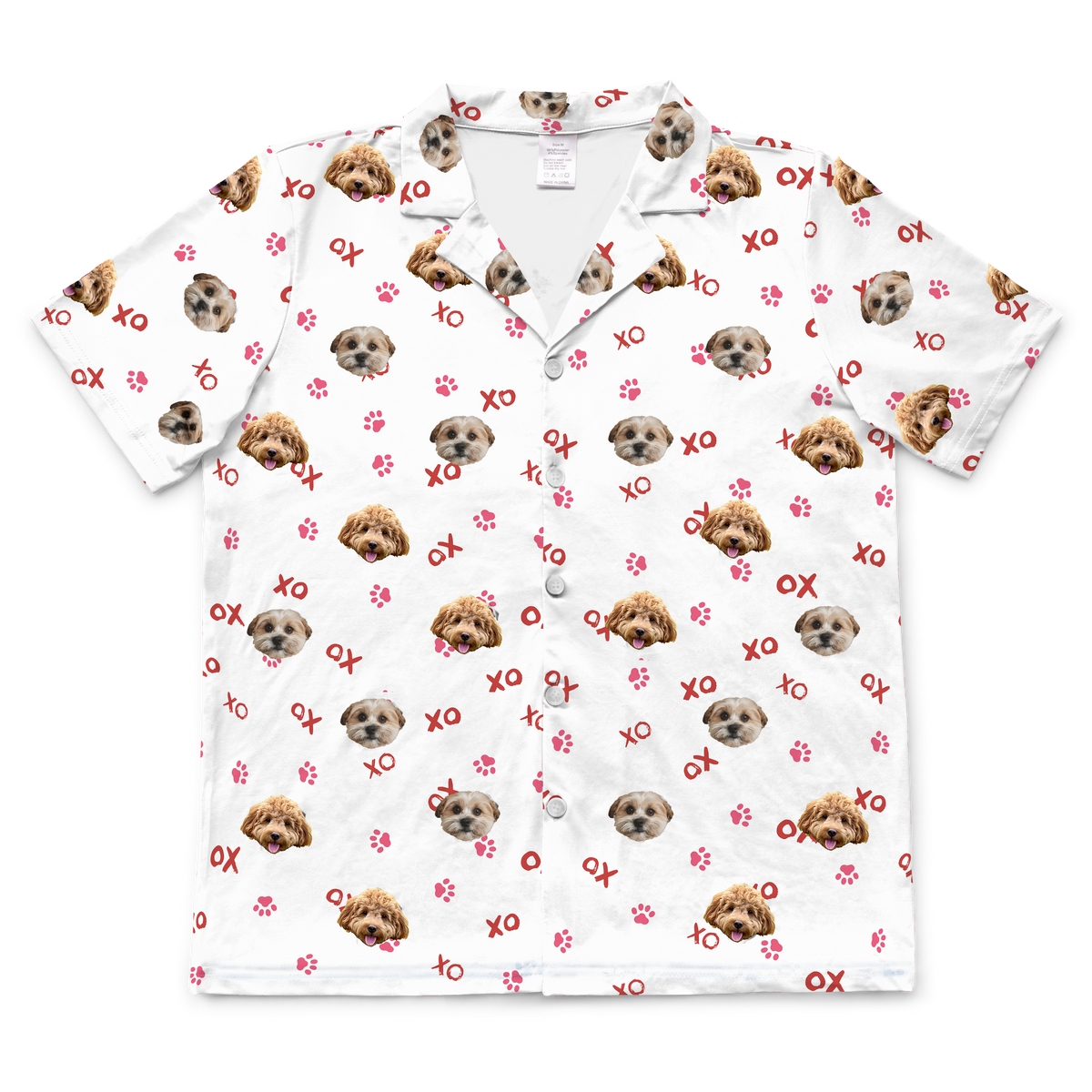 A white, short-sleeved pajama top with a button-down front and collar. The top features a pattern of three different dogs' faces—one reddish-brown, one light brown, and one mostly white/light tan—along with scattered red "XO" text and red paw prints.