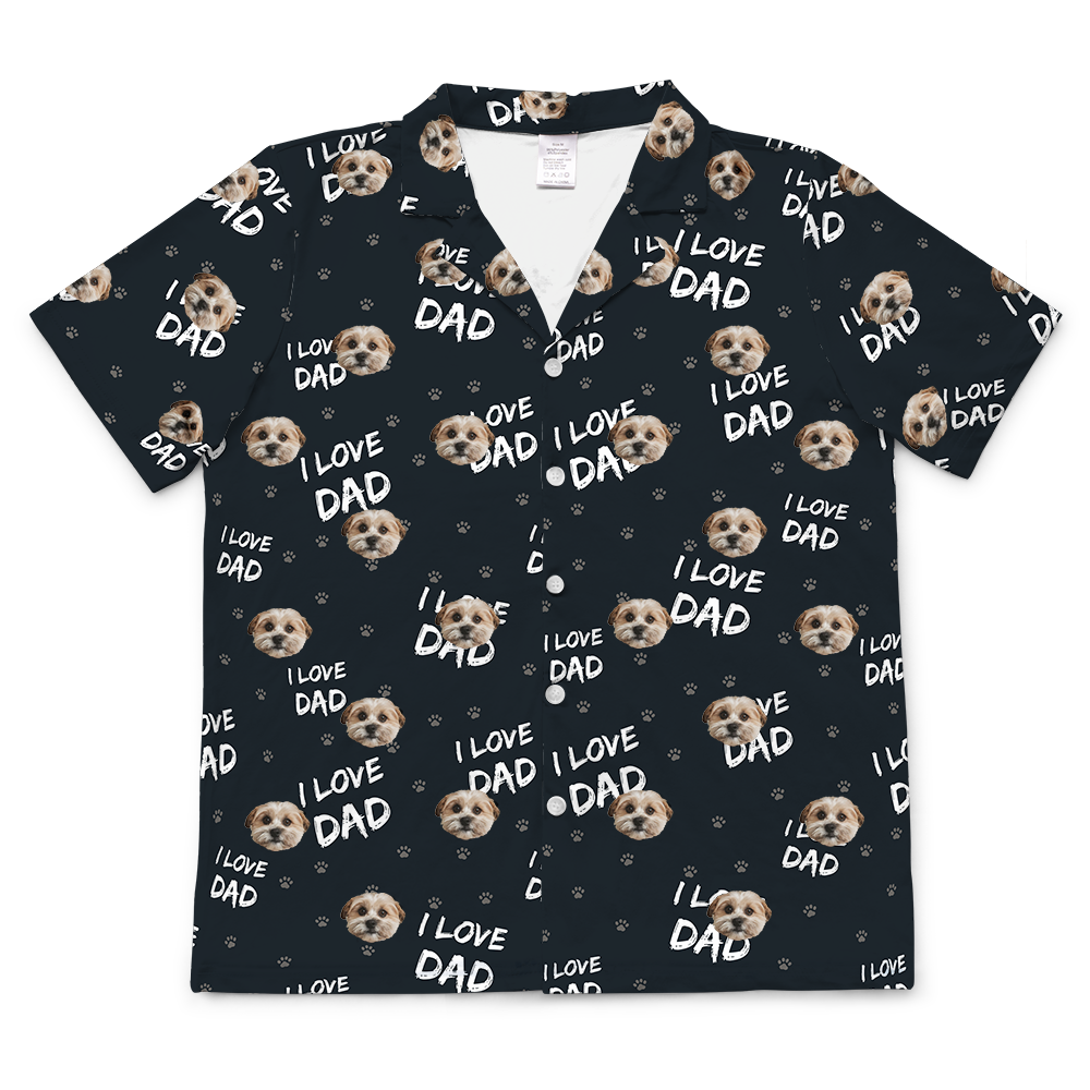 Black short-sleeve button-down pajama top with an all-over print of a dog’s face, gray paw prints, and the phrase “I LOVE DAD” in white lettering.