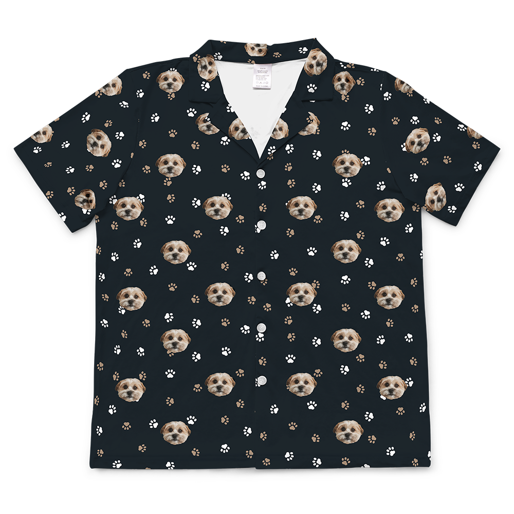 Short-sleeve button-down pajama top in black, patterned with white and brown paw prints and the custom photo head of a single, light-colored dog.