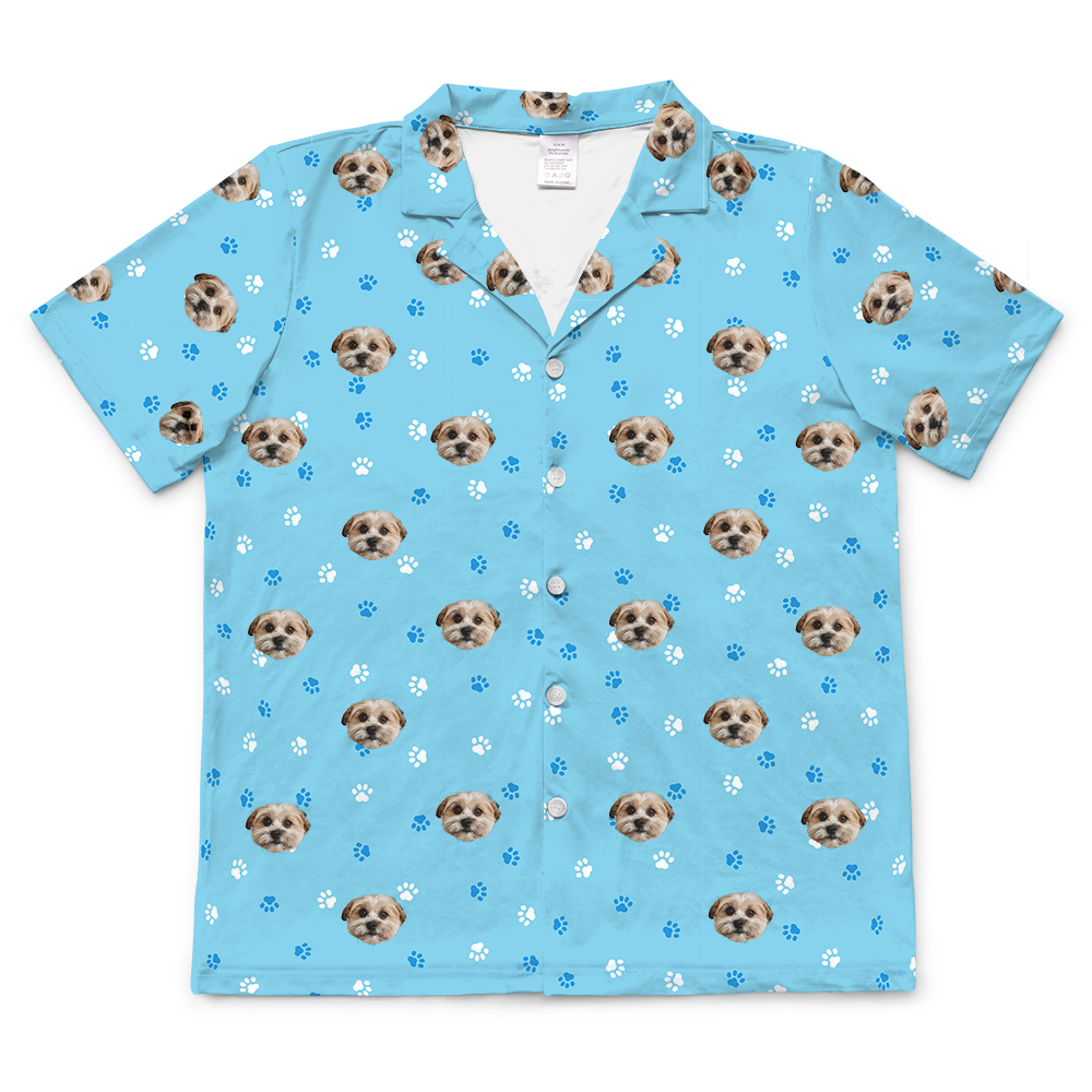 Light blue short-sleeve button-up pajama top featuring an all-over pattern of a small dog’s face with blue and white paw prints scattered throughout.