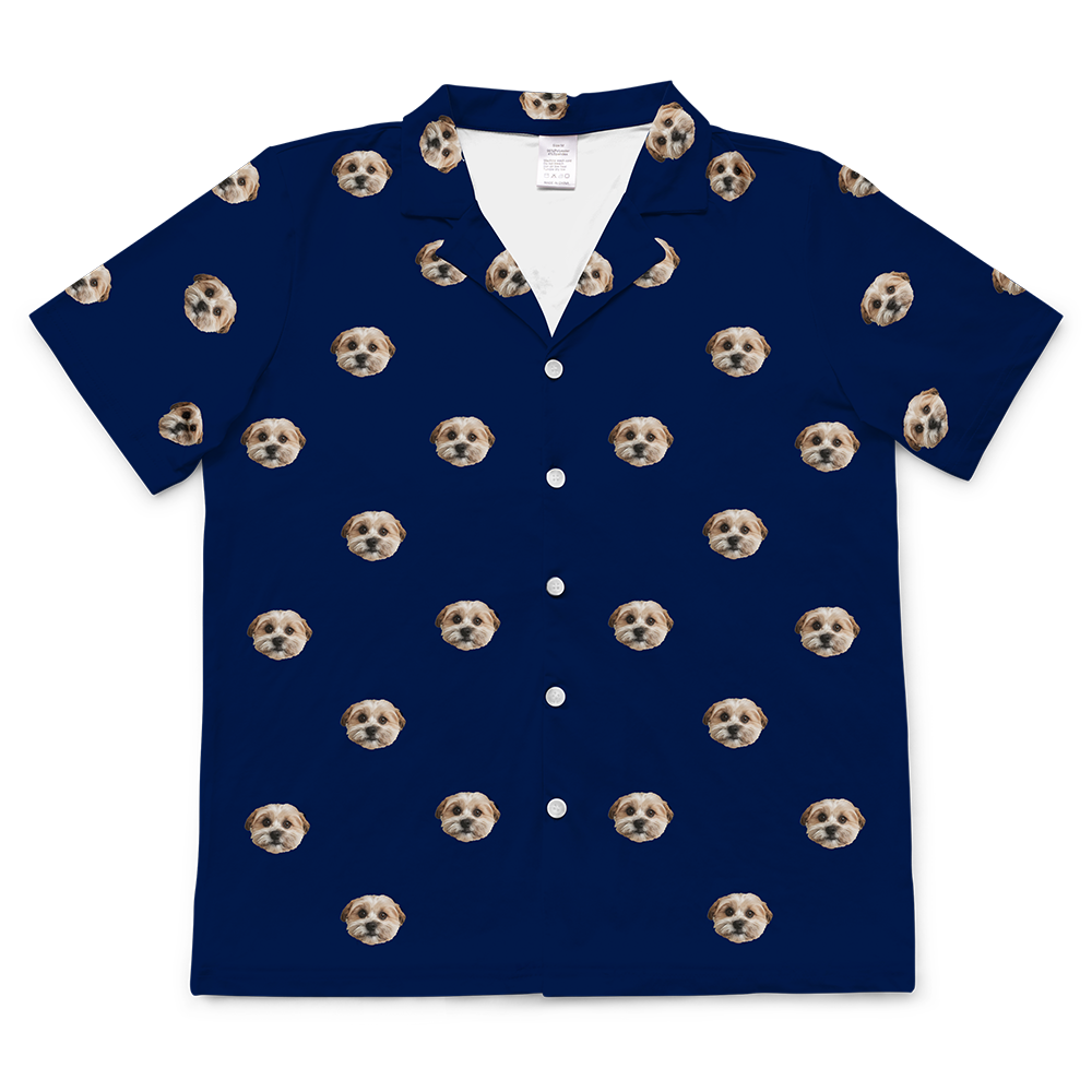 
A navy blue short-sleeve pajama top featuring a repeating pattern of light brown and white dog faces scattered across the fabric. The shirt has a notched collar and three white buttons visible down the front placket.