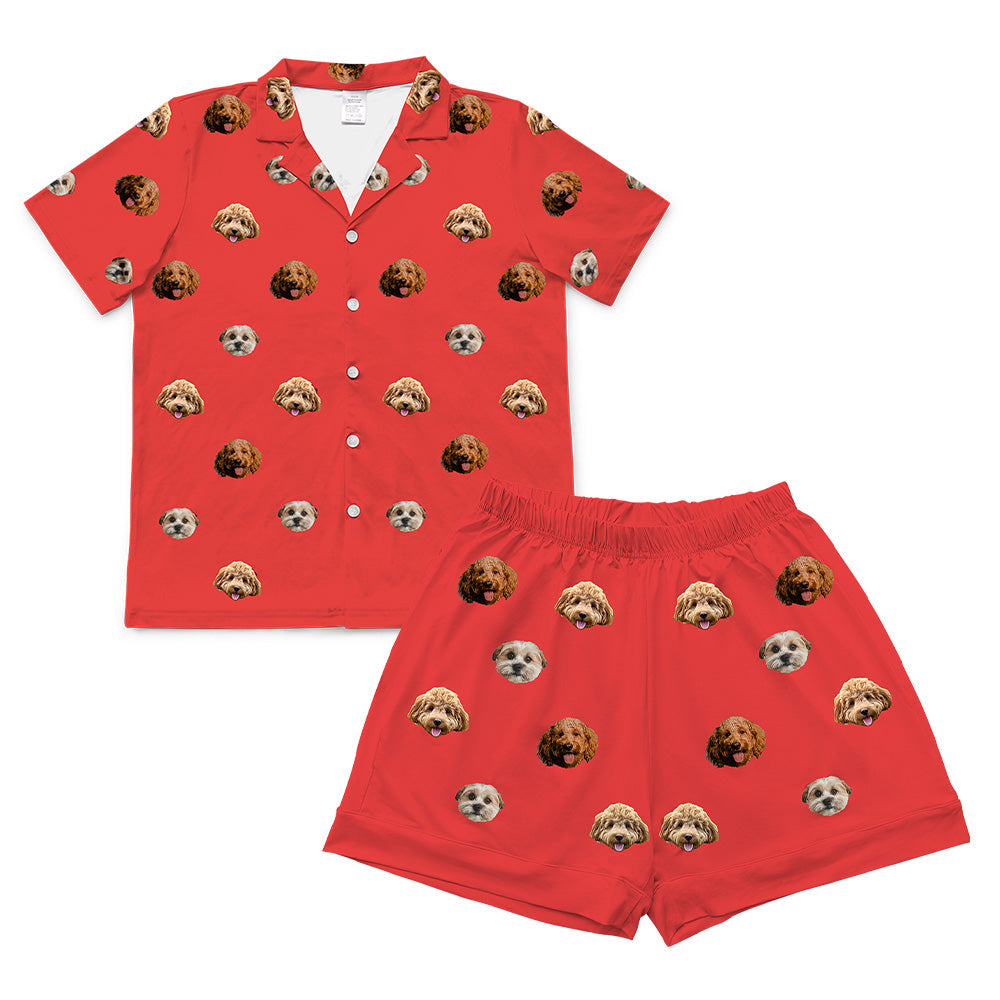 A matching short-sleeve pajama set (shirt and shorts) in a solid vibrant red color. The fabric is covered in a repeating, all-over pattern of small, cropped dog faces.