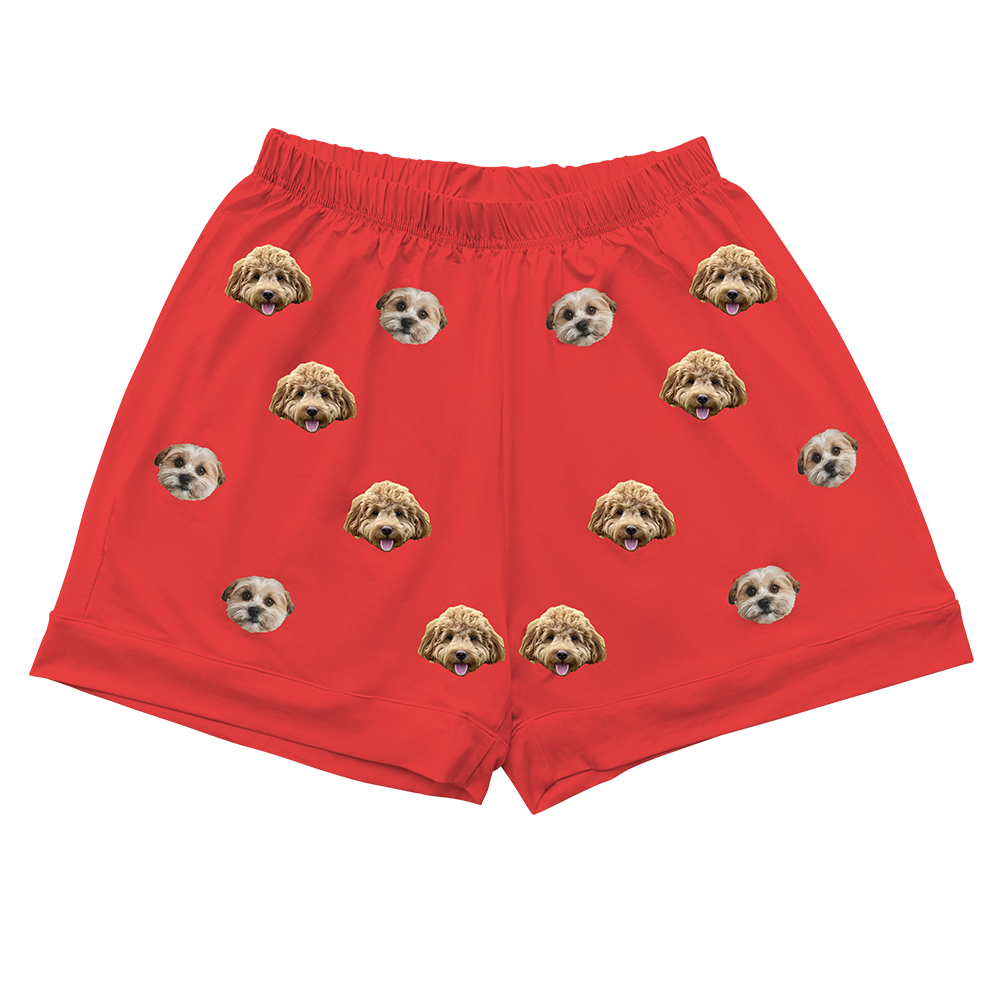 Close-up of a pair of red pajama shorts with an elastic waistband, featuring an all-over repeating pattern of two different dog faces.