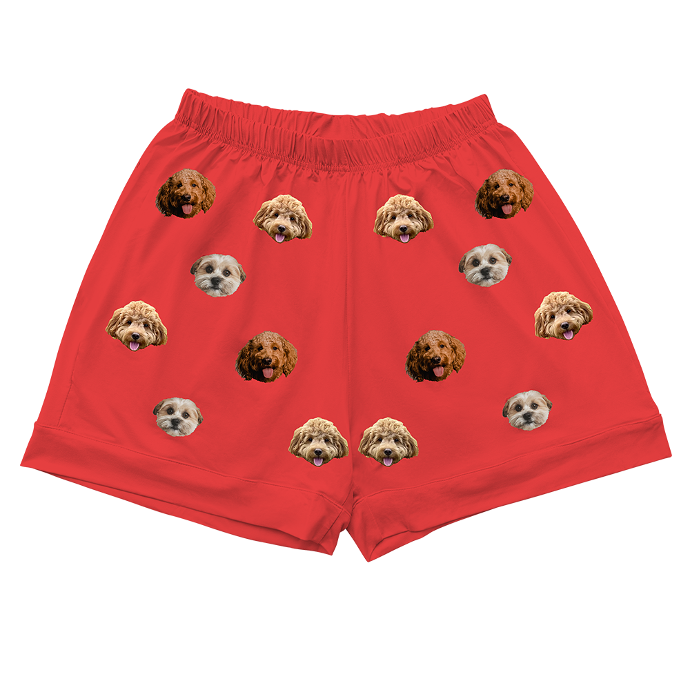 Close-up of a pair of red pajama shorts featuring an elastic waistband and an all-over repeating pattern of three different types of dog faces.