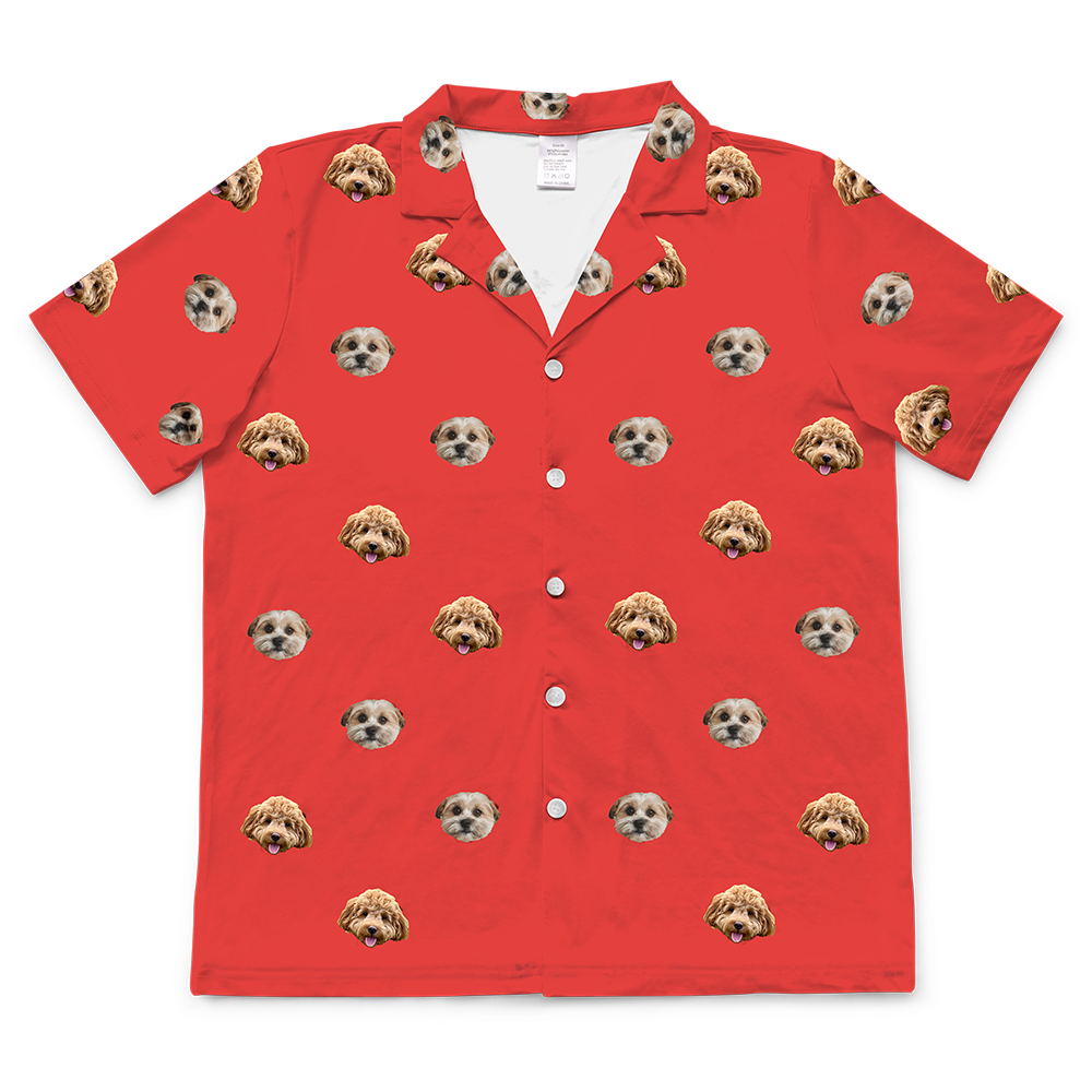 A single short-sleeve, button-down pajama shirt in a solid vibrant red color. The fabric is covered in a repeating, all-over pattern of small, cropped dog faces, featuring two different dog types.