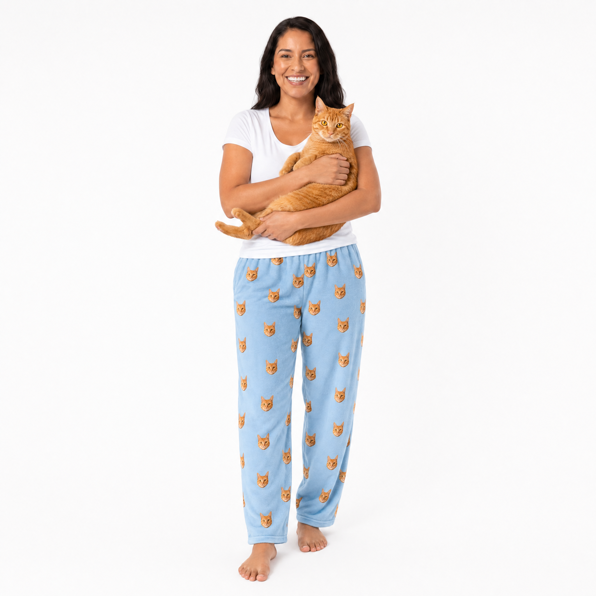 Woman wearing sky blue pajama pants with cat pattern, holding an orange cat on a white background