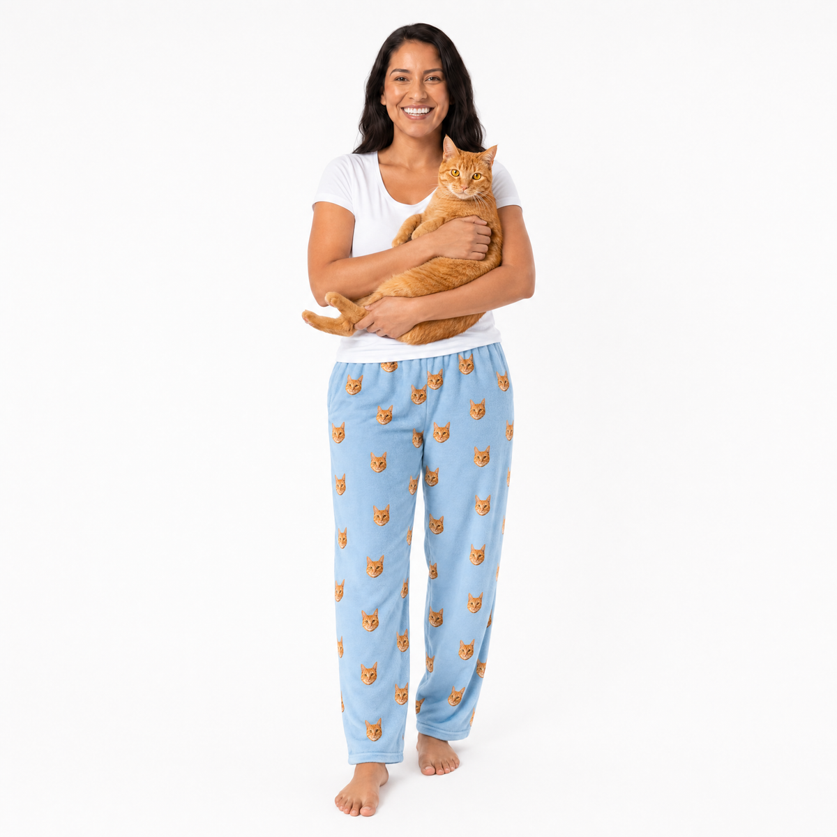 Woman wearing sky blue pajama pants with cat pattern, holding an orange cat on a white background