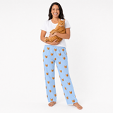 Woman wearing sky blue pajama pants with cat pattern, holding an orange cat on a white background