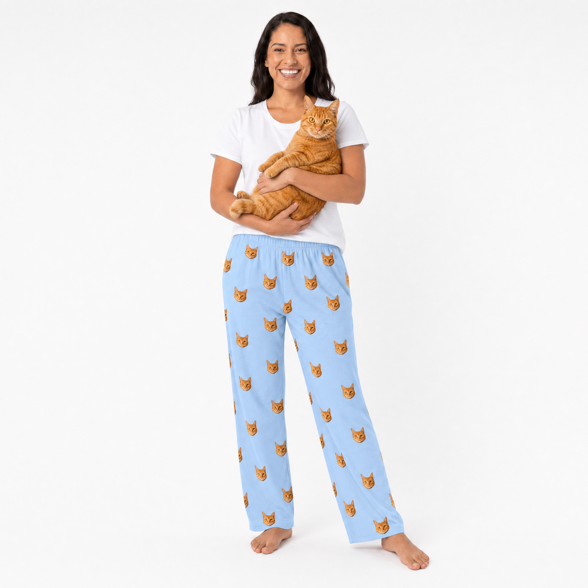 Woman wearing sky blue pajama pants with cat pattern, holding an orange cat on a white background