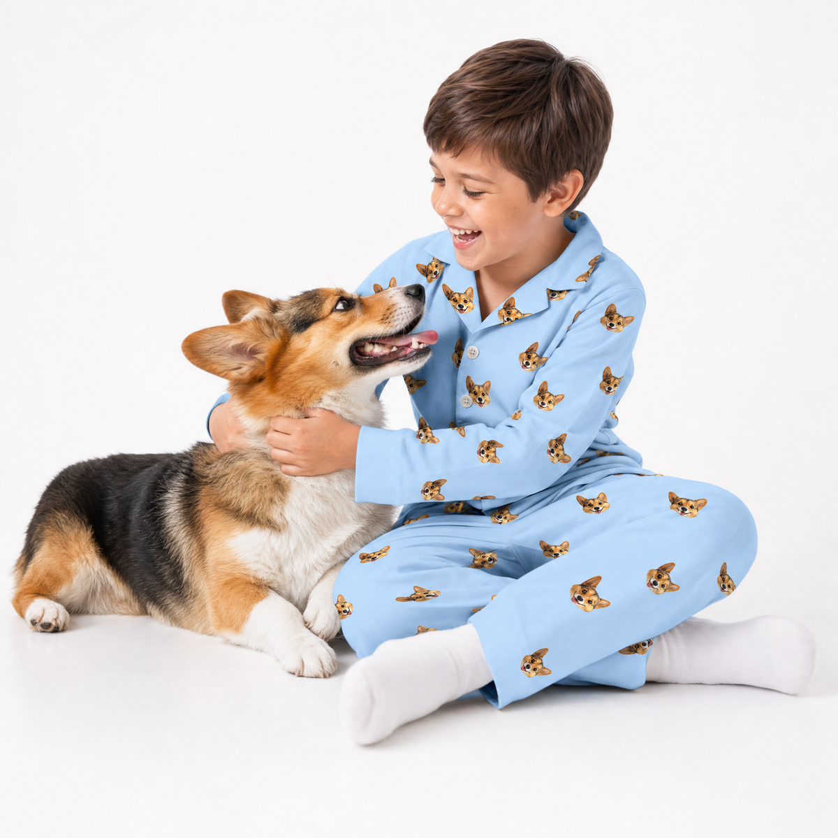 Child in sky blue pajamas with dog pattern sitting on a white surface with a dog.