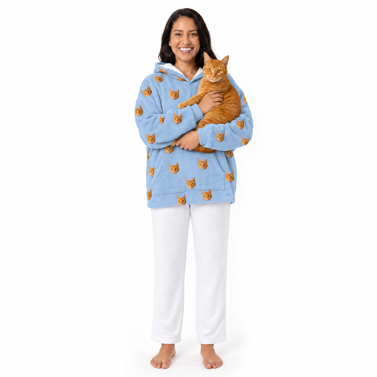Woman wearing a sky blue blanket hoodie with cat patterns, holding an orange cat on a white background
