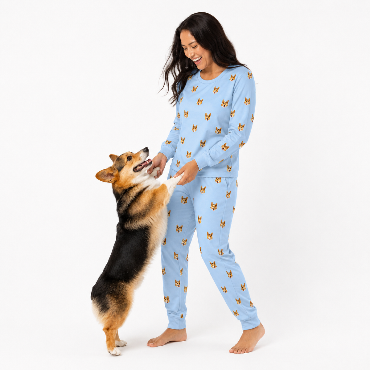 Woman in blue jogger pajamas with dog pattern standing next to a dog on a white background