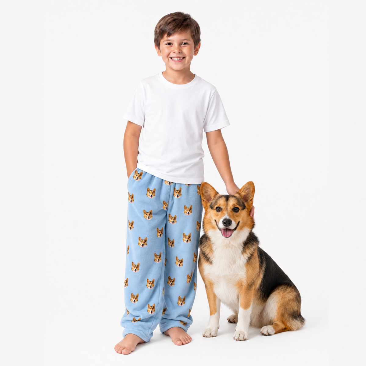 Child wearing sky blue pajama pants with dog pattern standing next to a dog on a white background