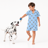 Child wearing a sky blue pajama set with dog pattern, standing next to a Dalmatian dog on a white background