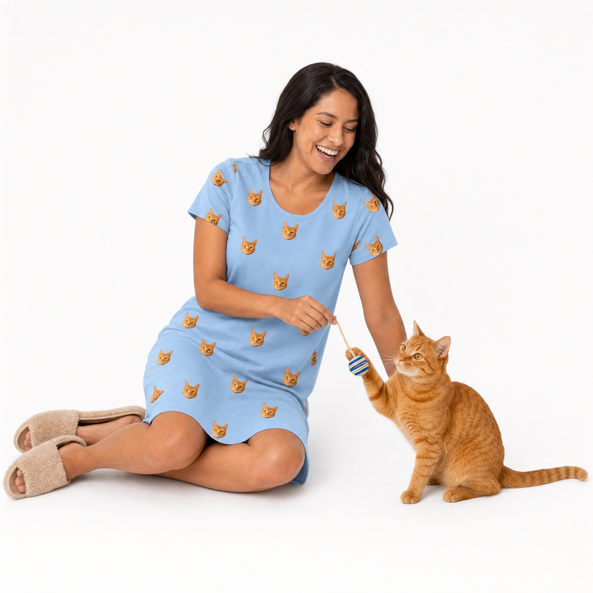 Woman in a sky blue nightgown with cat patterns sitting on the floor with a cat.