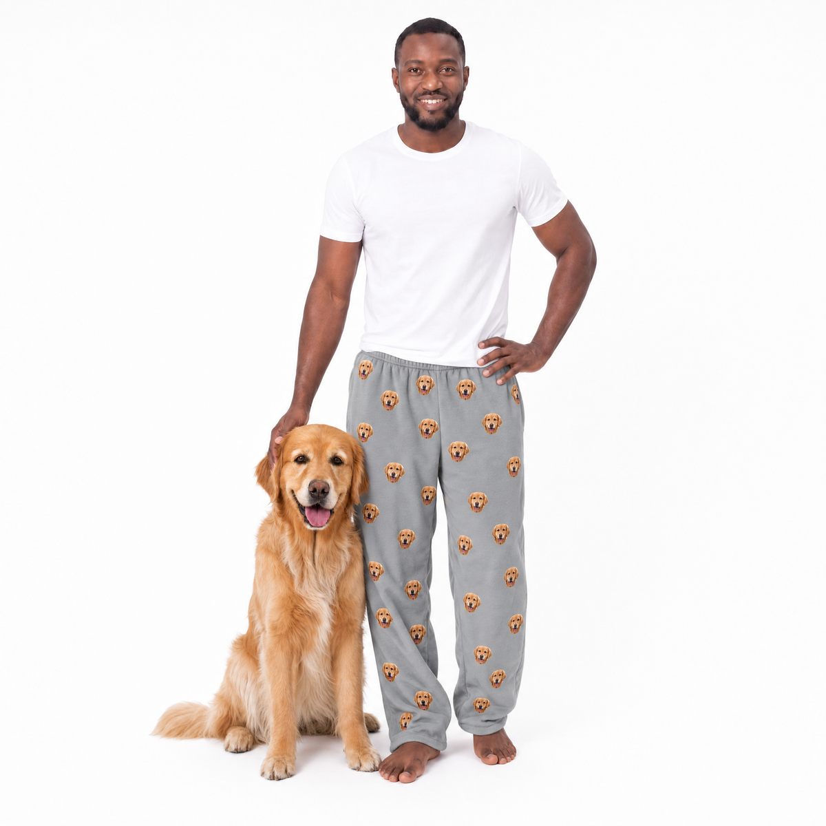 Man wearing gray pajama pants with dog prints, standing next to a dog on a white background