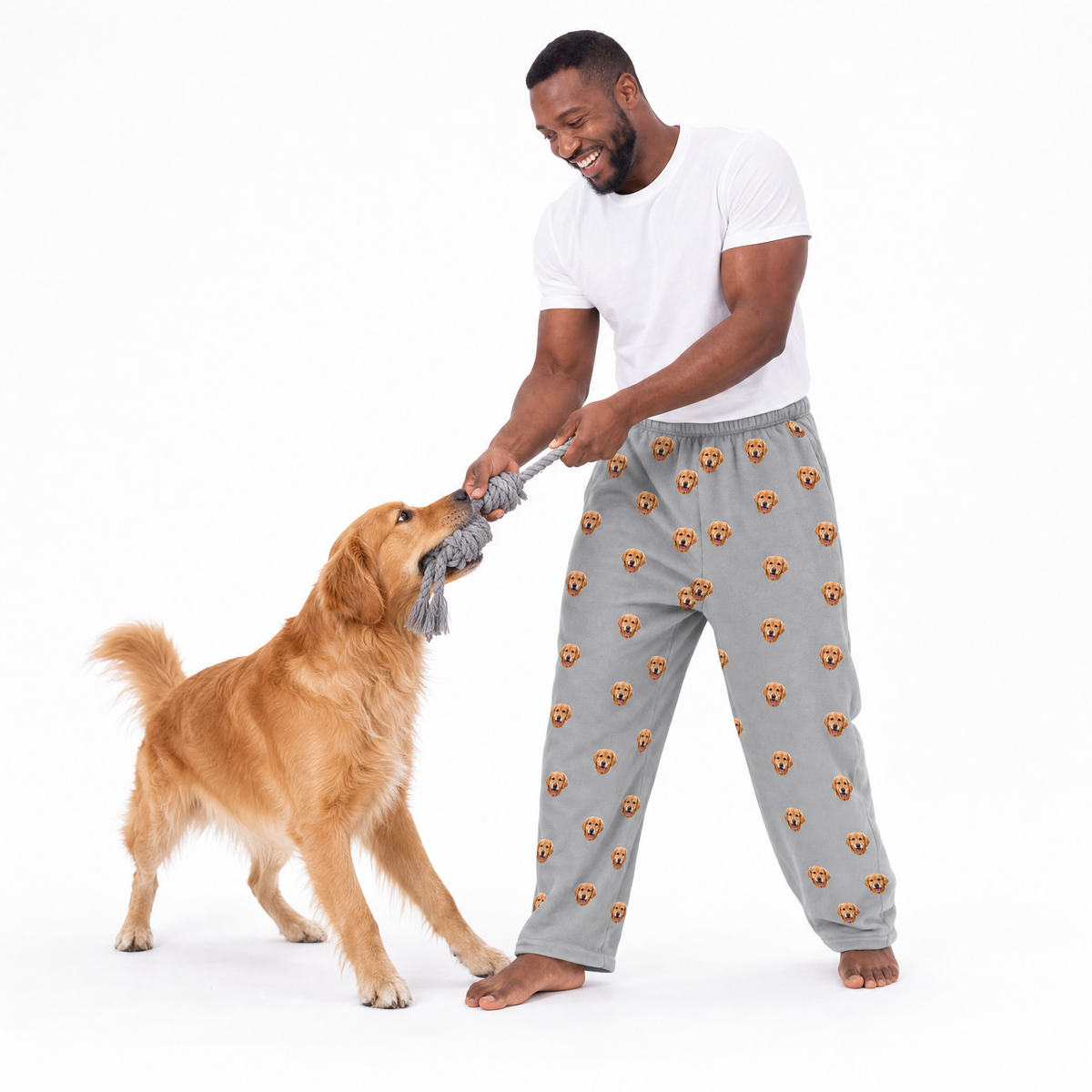 Man playing with a dog wearing pajama pants with dog patterns on a white background