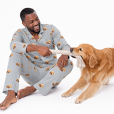 Man wearing a slate gray Golden Retriever print long sleeve pajama set while sitting on the floor and smiling as he plays tug-of-war with a Golden Retriever using a rope toy.