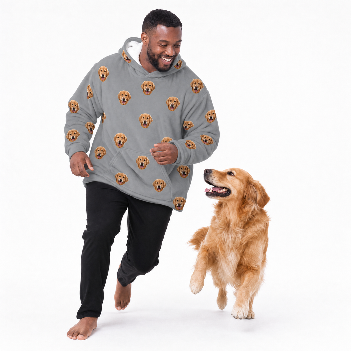 Man wearing a gray blanket hoodie with dog face patterns, standing next to a dog on a white background