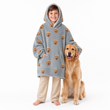 Child wearing a gray blanket hoodie with dog pattern and beige pants, standing next to a golden retriever on a white background