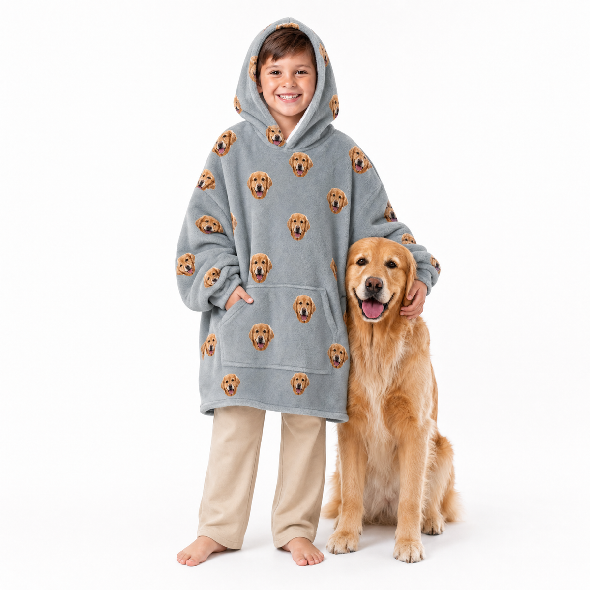 Child wearing a gray blanket hoodie with dog pattern and beige pants, standing next to a golden retriever on a white background