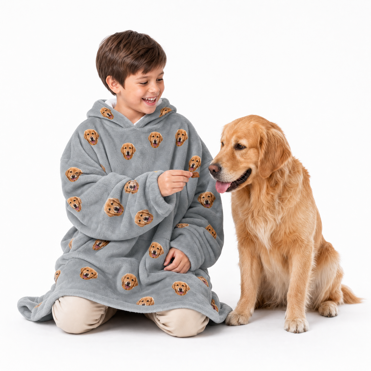 Child wearing a gray blanket hoodie with dog patterns, sitting next to a golden dog on a white background
