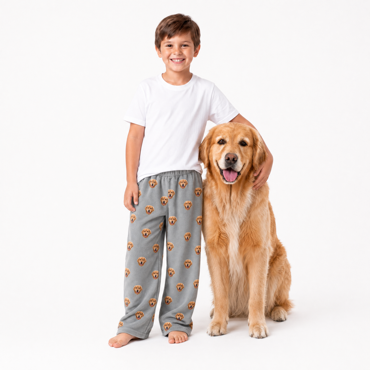 Child wearing gray pajama pants with dog pattern standing next to a golden retriever dog on a white background