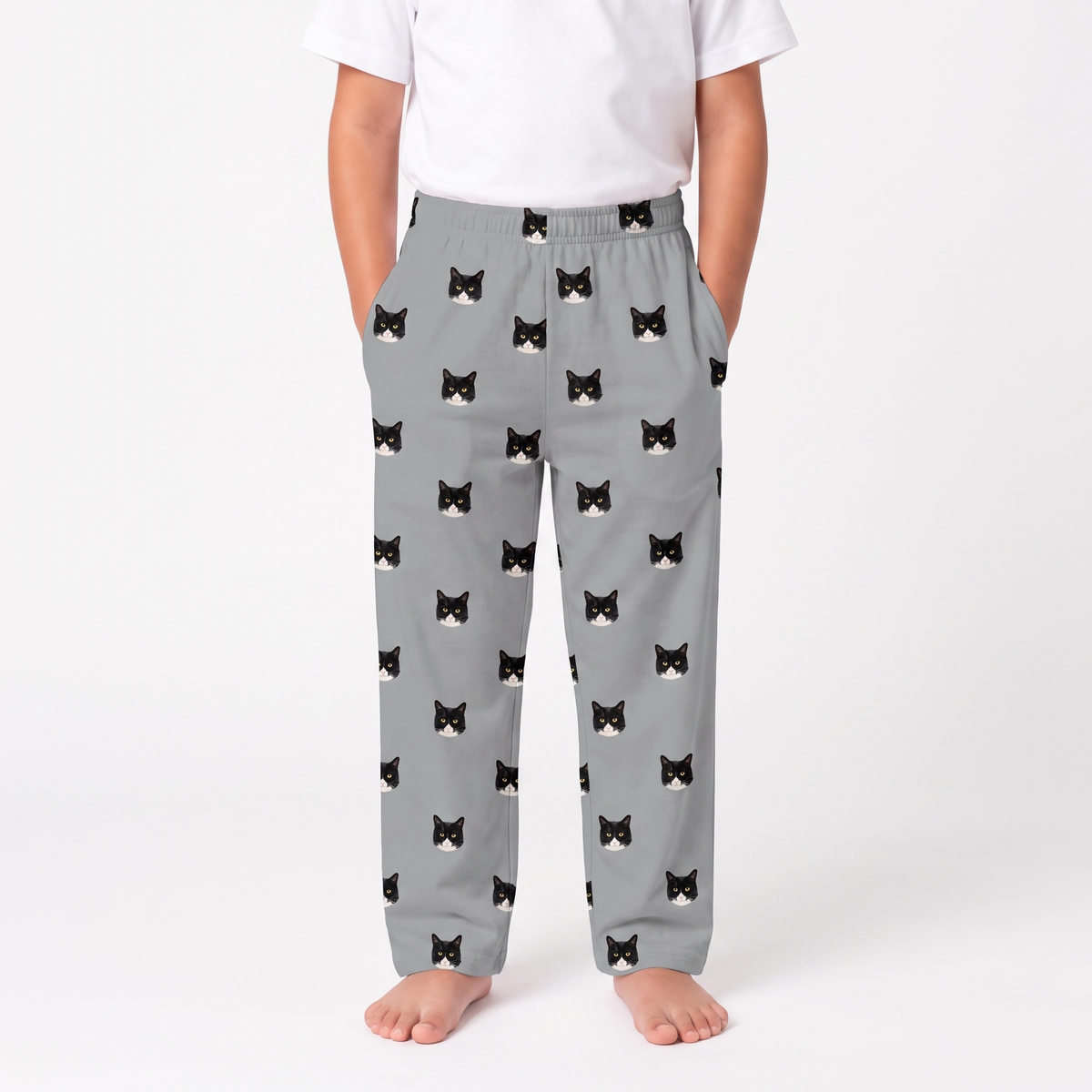 A child wearing slate gray pants with an all-over black and white cat face print, paired with a white t-shirt, shown against a plain white studio background.