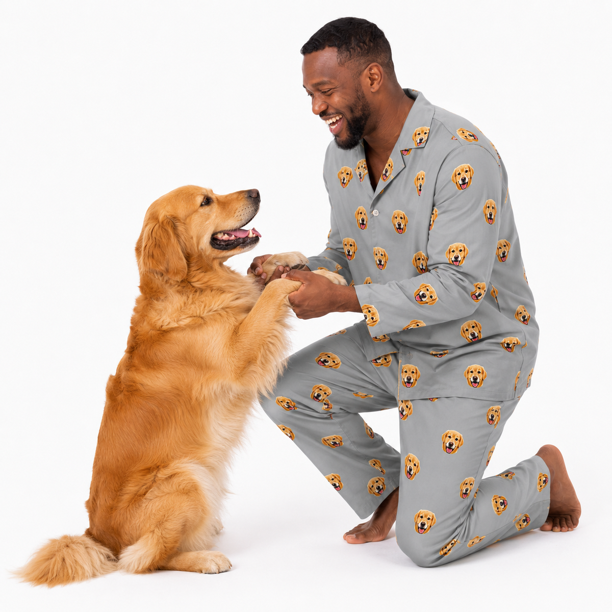 Man wearing a Slate Gray dog-print pajama set kneeling and holding paws with a golden retriever.