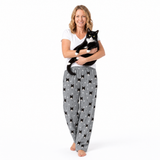 Woman wearing gray pajama pants with black cat patterns, holding a black and white cat on a white background