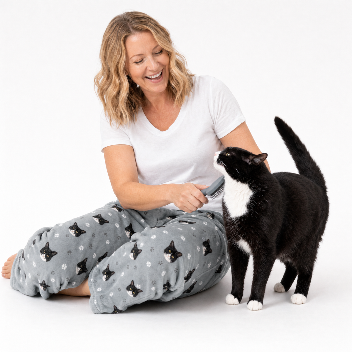 Woman brushing a black and white cat on a white background