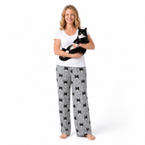 Woman wearing a white top and gray cat patterned pants holding a black and white cat on a white background