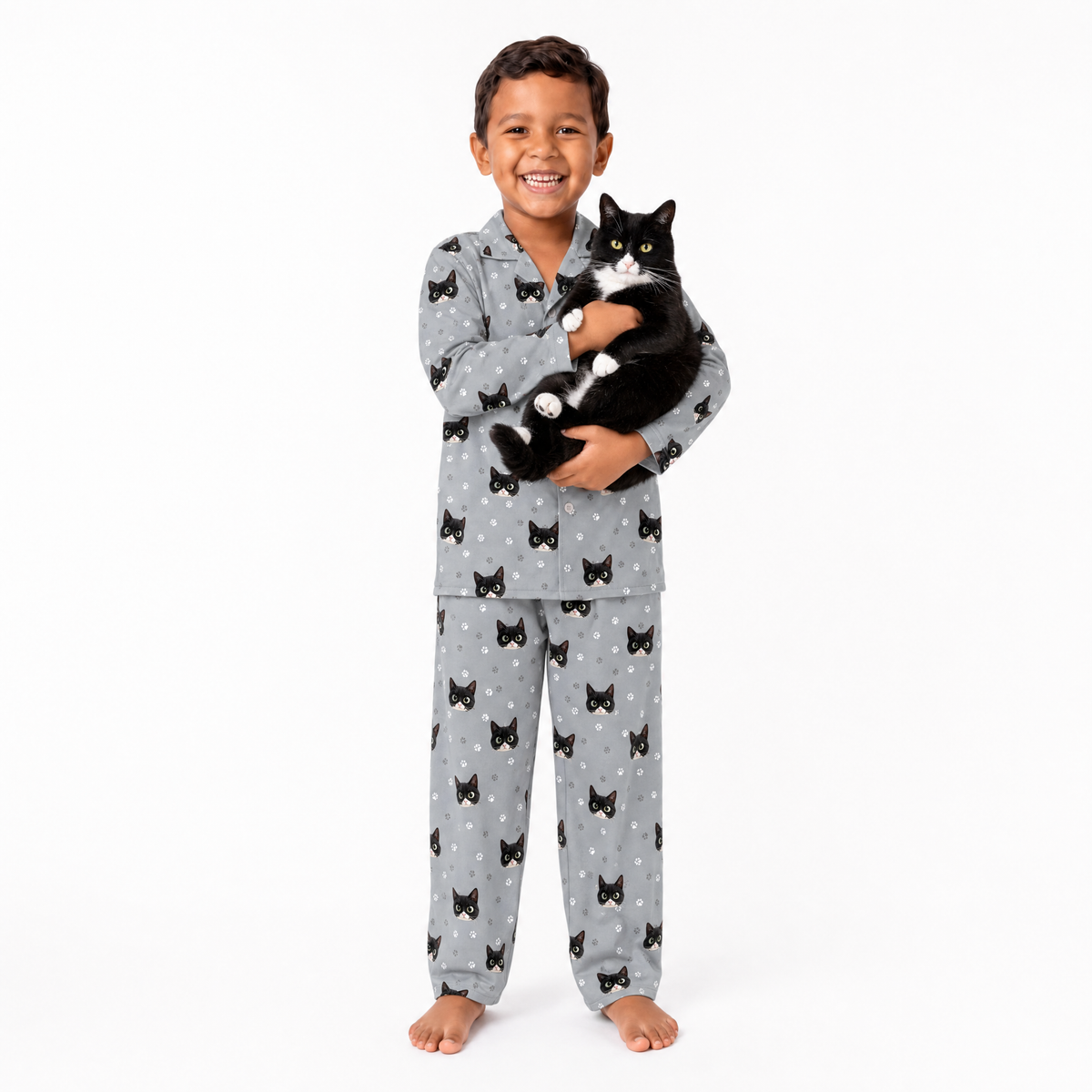 Child wearing gray pajamas with black cat patterns, holding a black and white cat on a white background