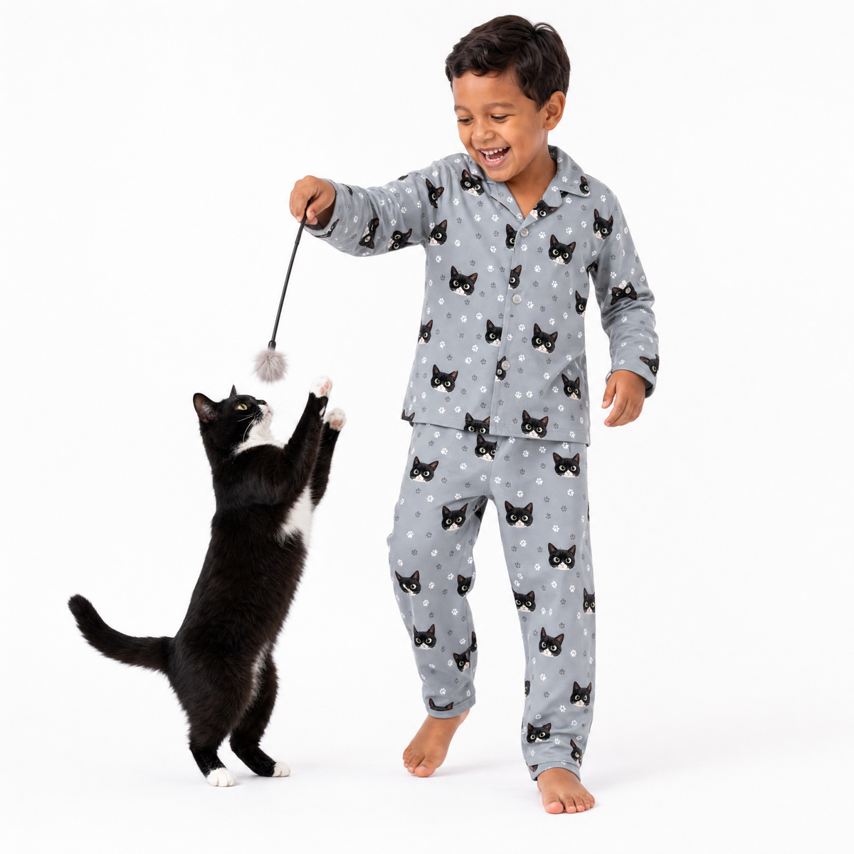 Child in gray pajama set with cat pattern playing with a black and white cat on a white background