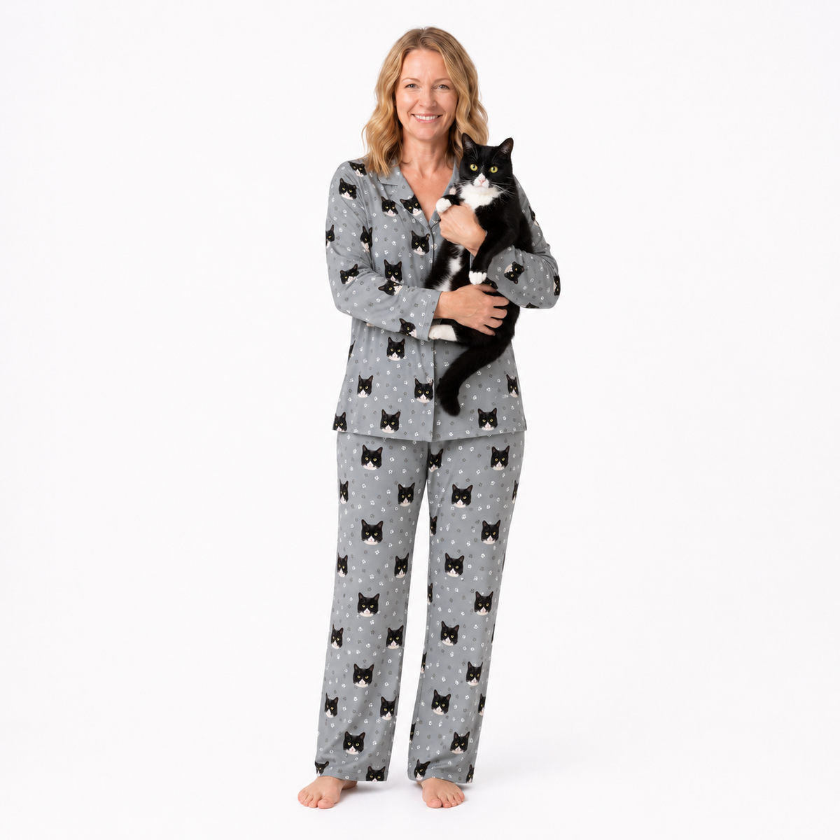Woman wearing gray pajamas with black cat patterns, holding a black cat on a white background