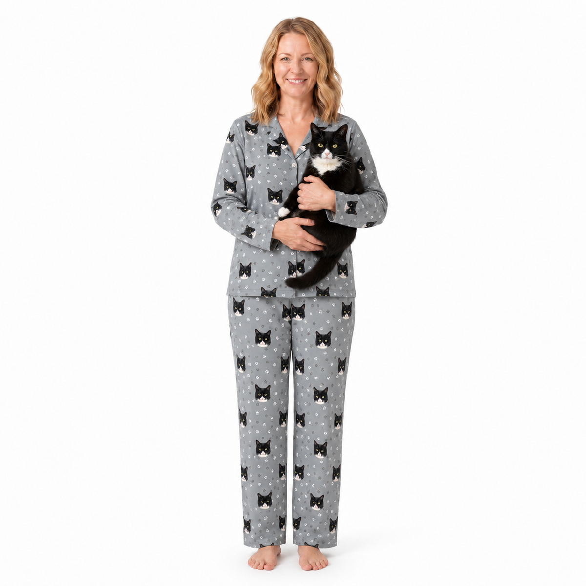 Woman wearing gray pajamas with black bow pattern, holding a black and white cat on a white background