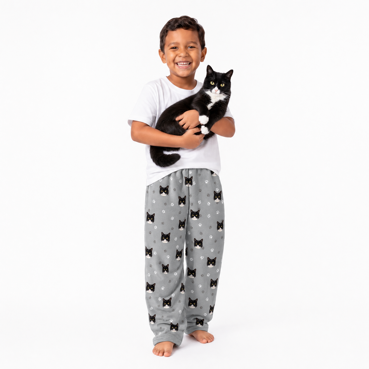Child wearing a white shirt and gray  pajama pants holding a black and white cat on a white background