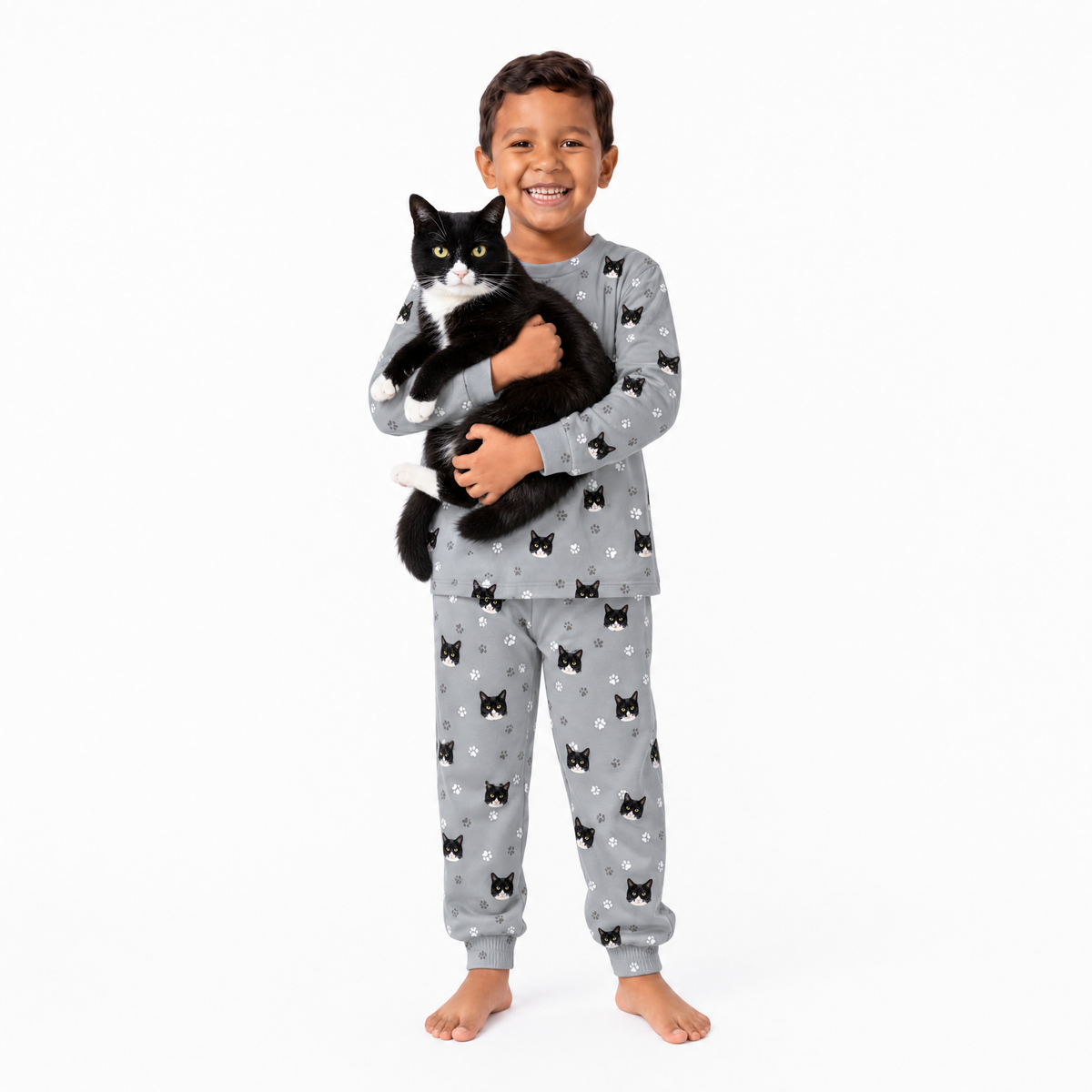 Child wearing a gray jogger pajama set with cat patterns, holding a black and white cat on a white background.