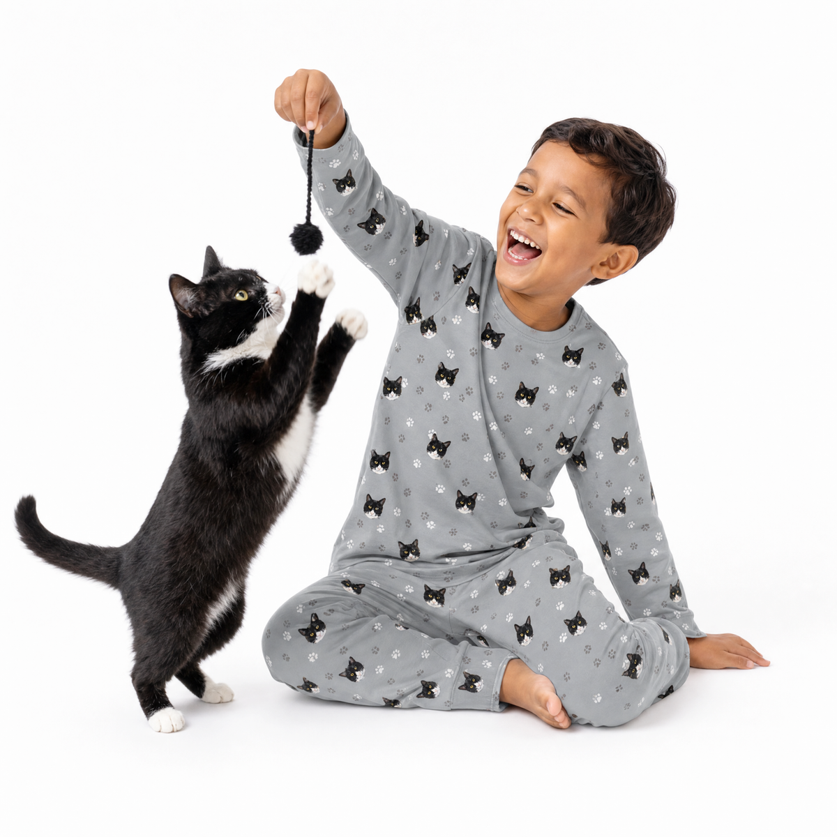 Child in gray jogger pajamas playing with a black and white cat on a white background