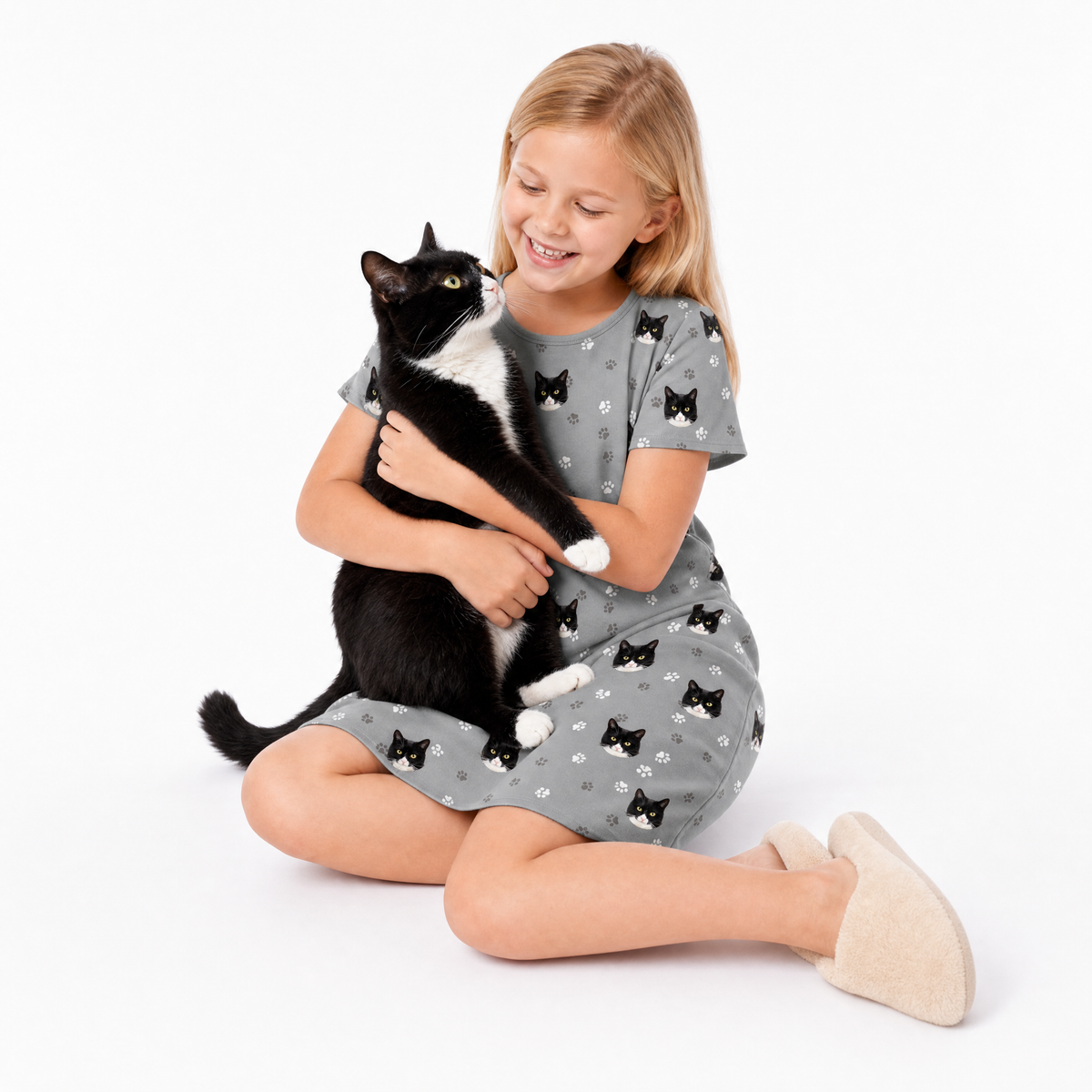 Girl in a gray nightgown with black cat patterns holding a black and white cat on a white background
